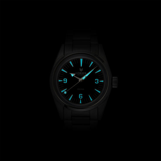 Lorier Falcon automatic watch in darkness showing Superluminova lume on Arabic numerals, baton hour markers, and handset glowing blue-green against black background.