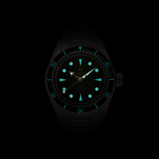 Lorier Neptune automatic dive watch in darkness showing Superluminova lume on hour markers, handset, and dive bezel numerals glowing blue-green against black background.