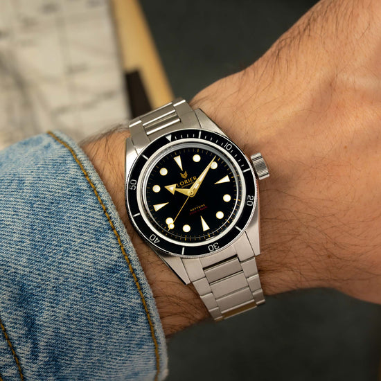 A Lorier Neptune watch with a black dial and stainless steel bracelet, shown worn on a person's wrist with a denim sleeve visible.
